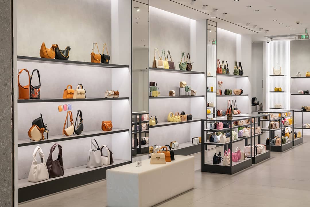 A modern luxury fashion store displaying handbags and purses in racks and tables at a shopping mall.